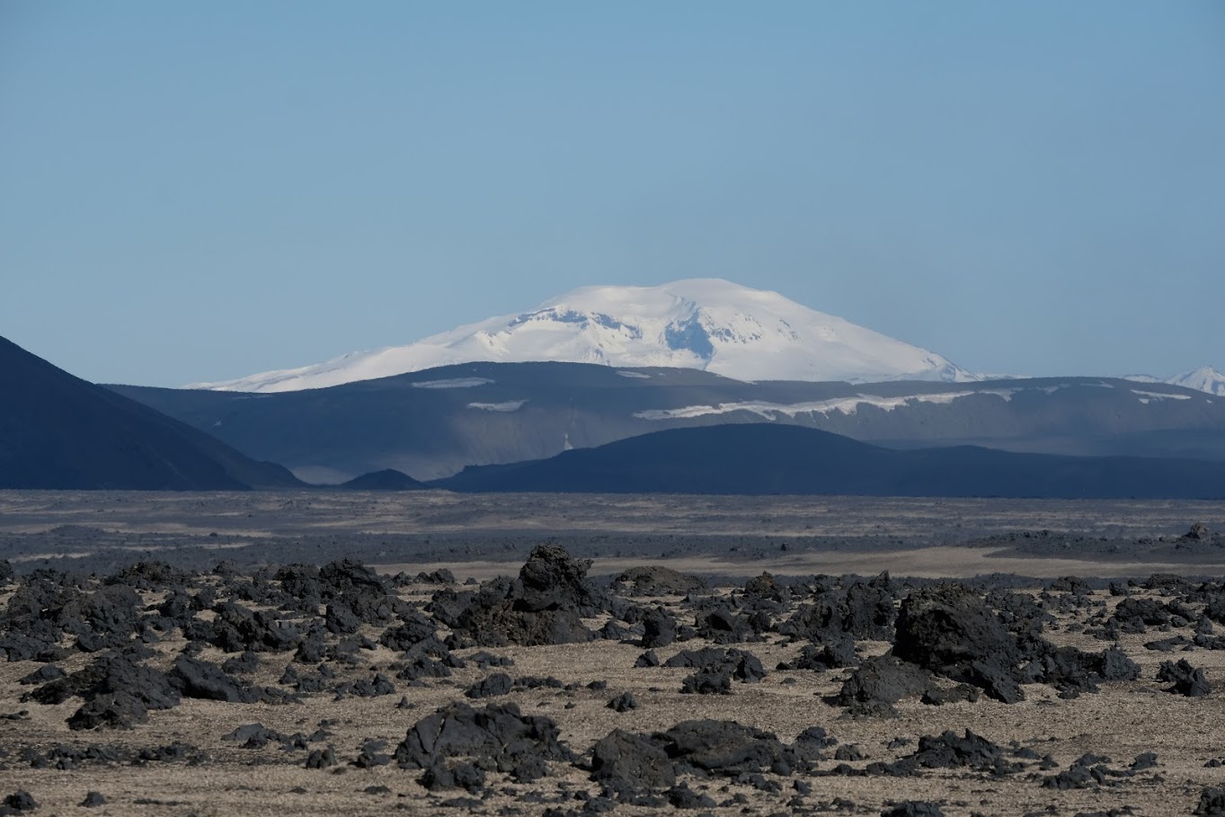 A snowy mountain in the distance, with rocky volcanic terrain in front